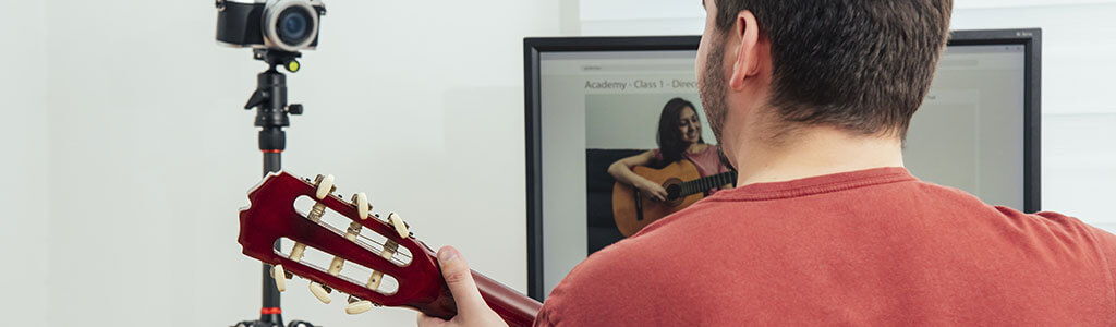Mann mit Gitarre nimmt an Online-Gitarrenunterricht teil - Lehrerin auf Bildschirm, Kamera für Videokonferenz